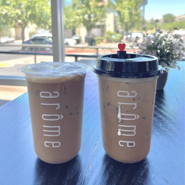 Two iced Arome Cafe drinks with the logo visible, on a table with an outdoor view.