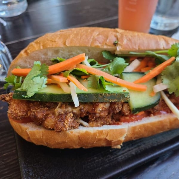 Close-up of a crispy fried chicken banh mi sandwich with pickled carrots, cucumbers, and cilantro.