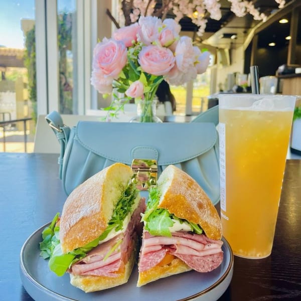 Arome Cafe's sandwich, cut in half, with a drink and a light blue purse on a table.